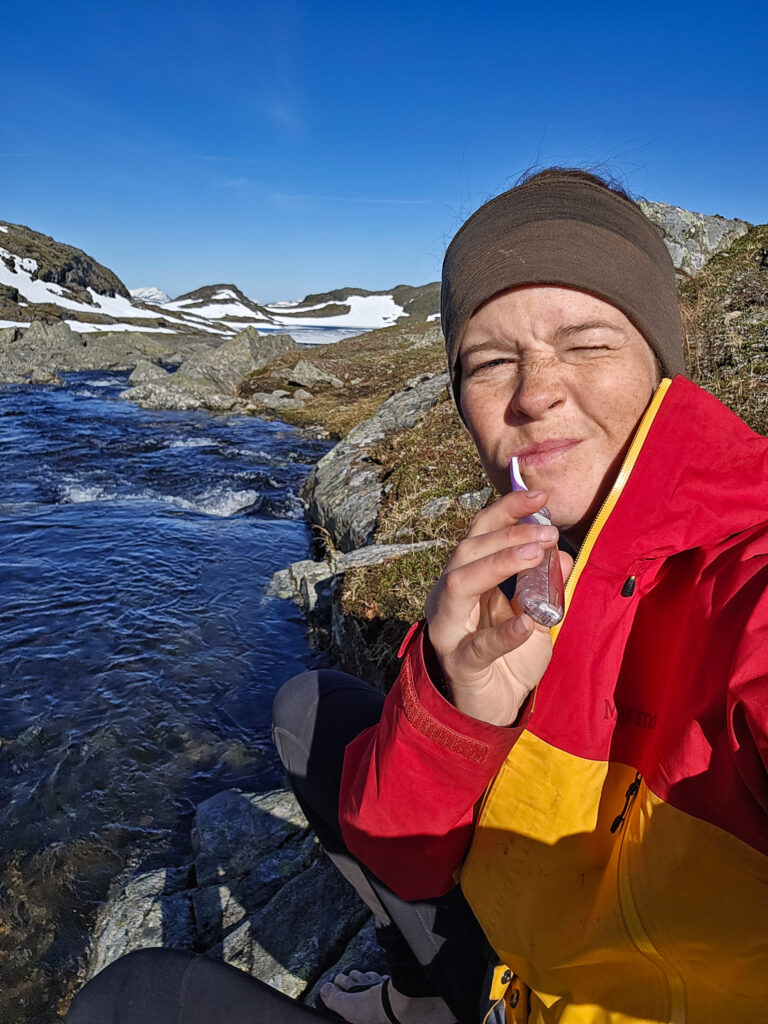 Wilda Nilsson borstar tänderna på fjället i rödgul jacka